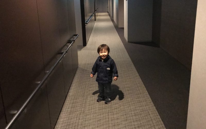 マンションの内廊下を新居の近所への引越し挨拶に向かう1歳児