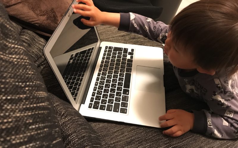ソファの上のパソコンを操作する1歳児