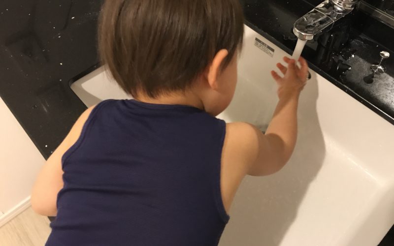洗面所の水道で手を洗う1歳児